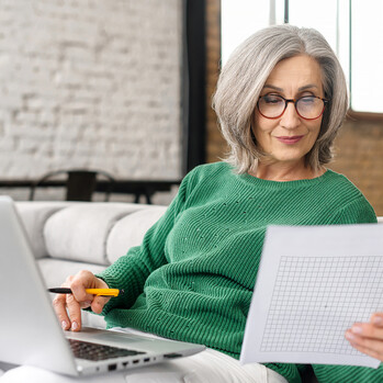 Frau mittleren Alters sitz mit Laptop auf der Couch und macht den Amsler-Gitter-Test