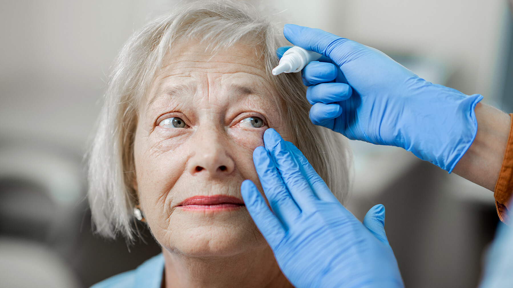 Medizinische Fachkraft träufelt Augentropfen in die Augen einer älteren Dame